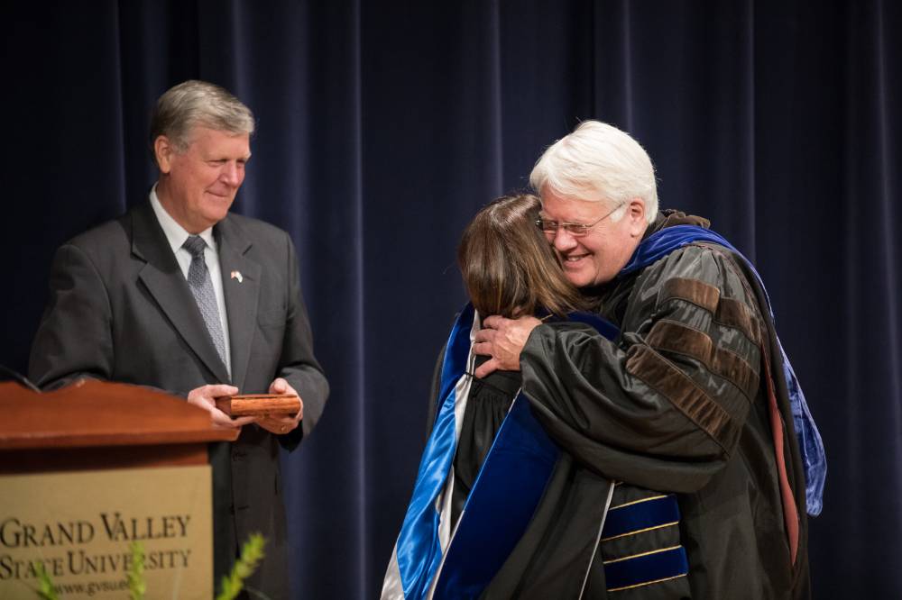 The Provost is hugging a faculty member while presenting the award to them.